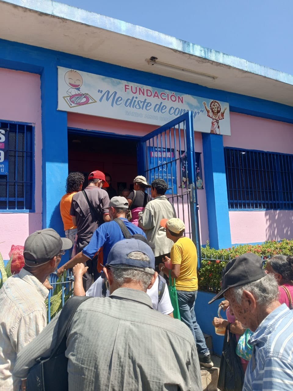 Personas hacen fila a la entrada del comedor de la Fundación Me Diste de Comer